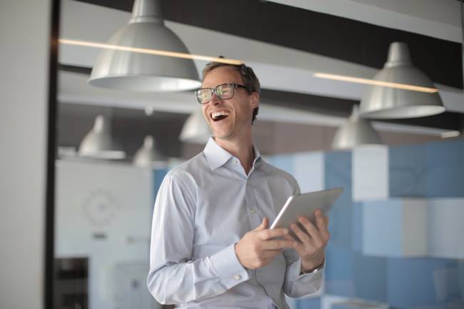 Ein Mann mit Tablet lacht fröhlich. Sein Unternehmen setzt erfolgreich auf KI, wie es der Future of Work Report: AI at Work vorschlägt. Bild: Pexels/Andrea Piacquadio