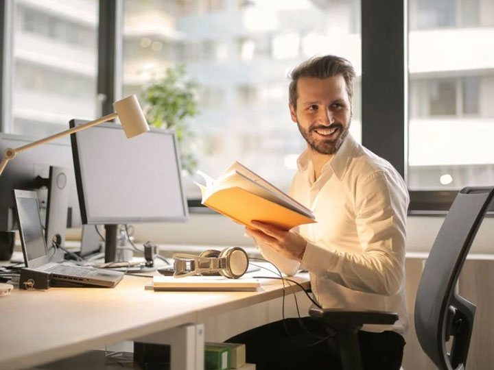 zu sehen ist ein lächelnder Mann in einem Büro an seinem Schreibtisch. Thema des Artikels ist die Wichtigkeit einer UTM-Firewall für ein sicheres Arbeiten. Bild: Pexels/Andrea Piacquadio